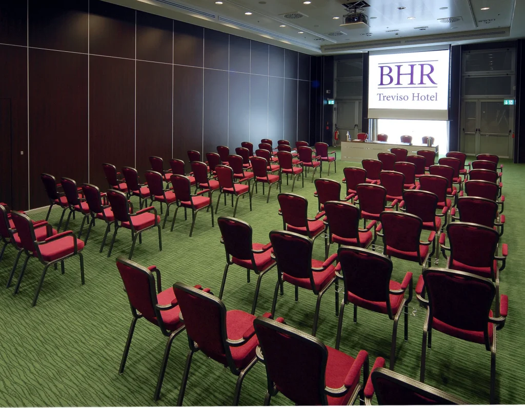 sala meeting con sedie disposte a teatro. Le sedie sono rosse e il pavimento è ricoperto di moquette verde